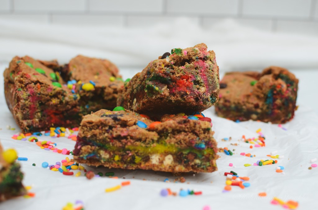 A close-up view of colorful rainbow blondies with sprinkles on a white surface, showcasing their layered texture and vibrant colors.