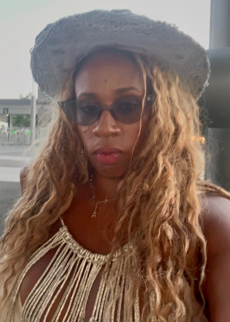 A person wearing a decorated cowboy hat and stylish outfit, standing outdoors.